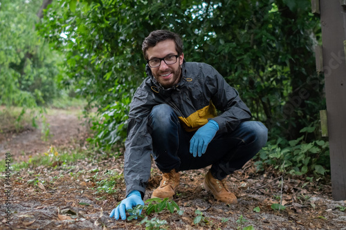 A young bearded man with brown hair and prescription glasses looks through the wilderness for specimens to collect for a study