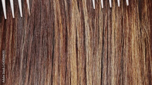 Young woman styling her long straight shiny dyed hair with comb, colored layers highlights, care concept, combing brunette hair, 4k