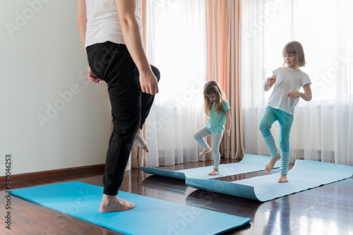 Home workout in flat.Dad teaching little girls fitness, daughters. Physical morning exercises on blue yoga mats.Family children fun.Healthy indoor activity.Quarantine,coronavirus covid-19.No equipment