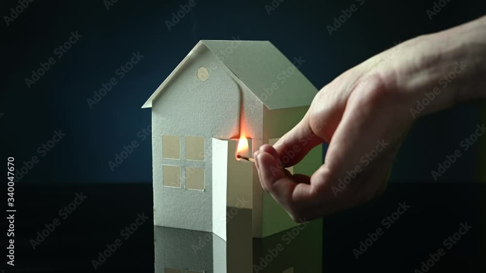 male hand sets a match on a paper house