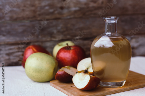 Apple organic vinegar in glass pitcher with ripe fresh red and yellow apples on wooden background. Healthy organic food concept
