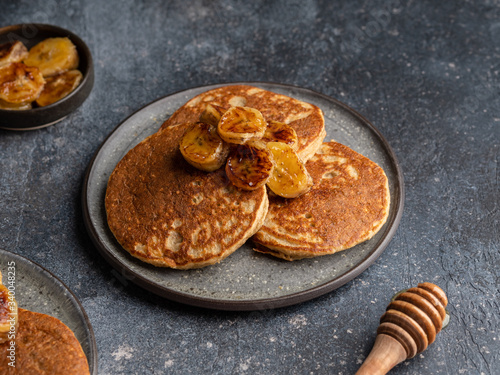 Oatmeal banana pancakes with honey and babana slices on ceramic plate. Healthy easy making morning breakfast. Homemade sugar free and gluten free food. Concrete background, top view. Copy space. photo