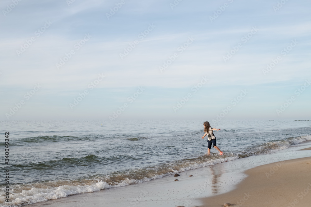 One long-haired girl running along the shore of the silver-colored North sea. Windy weather, Northern landscape, pastel color.