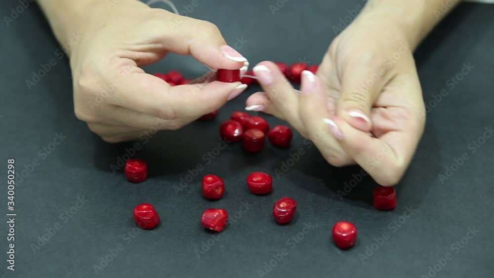 Close-up of hand of needlewoman making necklace of natural coral Close-up of hand of needlewoman making necklace of natural coral