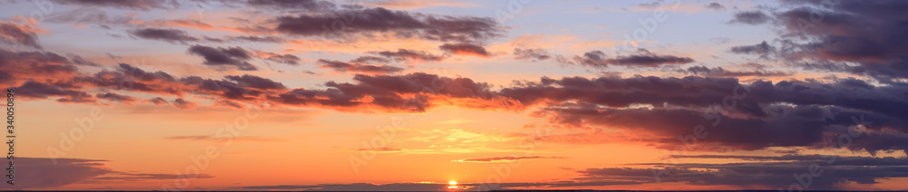 panorama view of colorful sky at sunset with the setting sun and orange yellow purple clouds in front of twilight and the last sunbeams, wide picture 