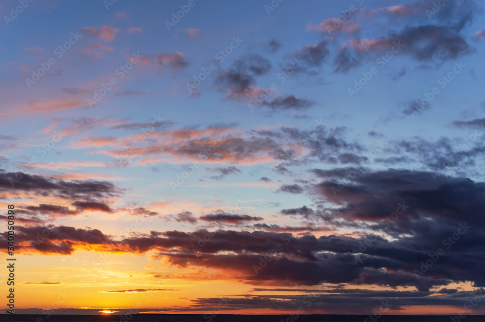 panoramic view of the colorful sky at sunset with the setting sun and orange yellow purple clouds in front of twilight and the last sunbeams