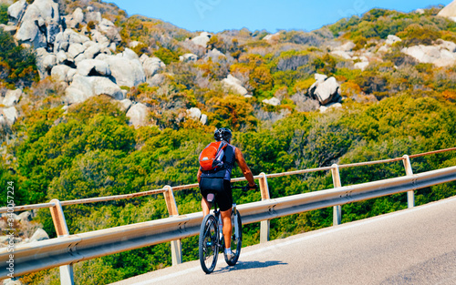 Man riding bicycle on road at rocks at Capo Testa reflex