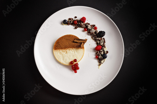Creme tiramisu tart with cocoa powder on top and chocolate crumps with berry fruits on the side. Amazing desert plating photography perfect for magazine and fine dine in menu concept.