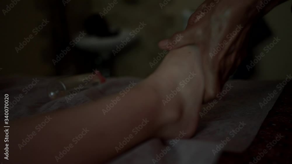 A professional thai masseur slowly massaging client’s leg with oil in a dark room, close-up. A spa client receiving a great relaxing thai massage. Warm film colors. A professional thai masseur slowly massaging client’s leg with oil in a dark room, close-up. A spa client receiving a great relaxing thai massage. Warm film colors.
