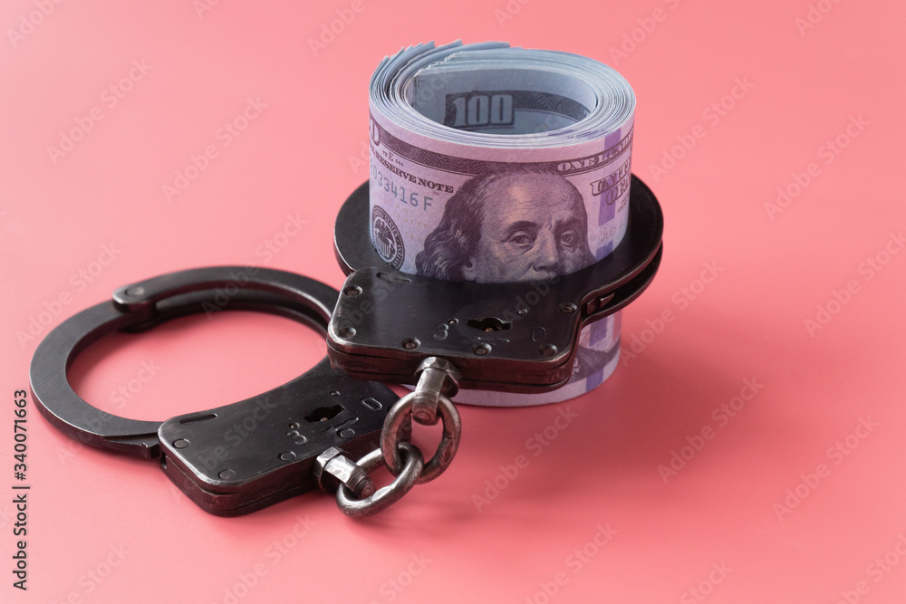 Obraz premium twisted wad of dollars buttoned with handcuffs on a pink background