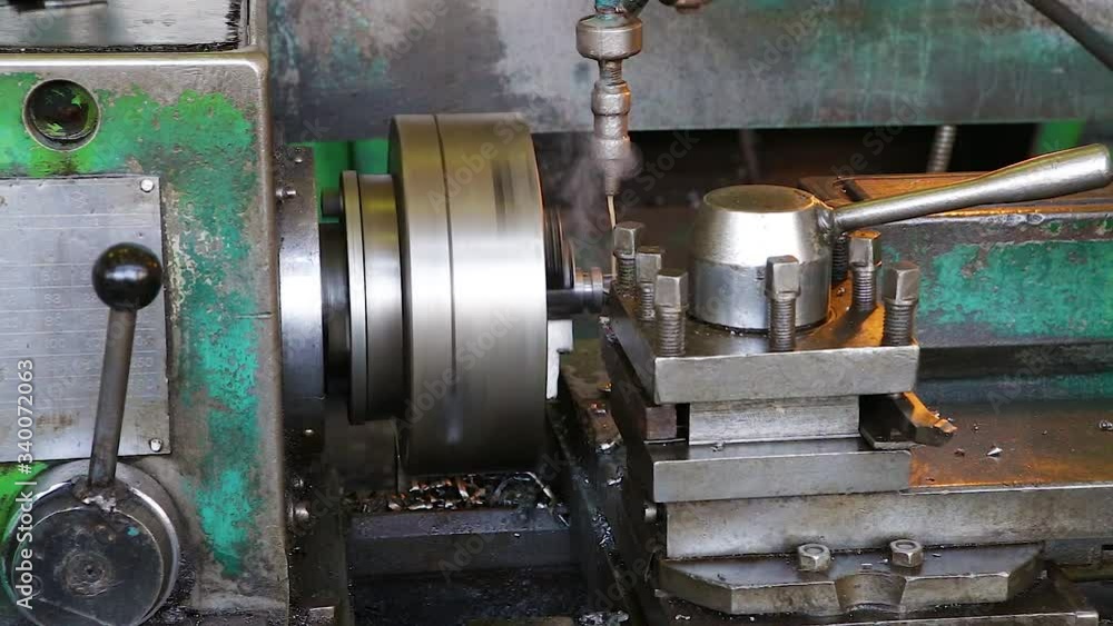 In an old lathe, chips are removed from a metal part. Water is poured onto the workpiece from above for cooling. Close-up In an old lathe, chips are removed from a metal part. Water is poured onto the workpiece from above for cooling. Close-up