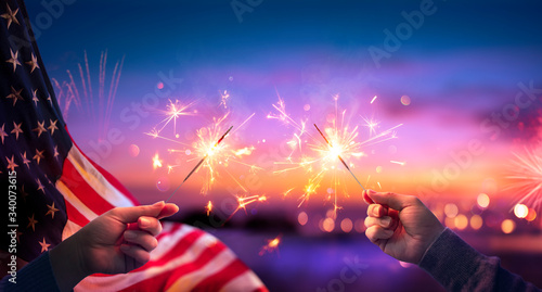 Usa Celebration - Hands Holding Sparklers And American Flag At Sunset With Fireworks
 photo