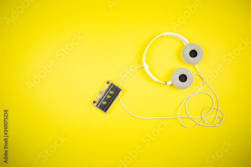 Audio cassette tape and modern headphones on a yellow background