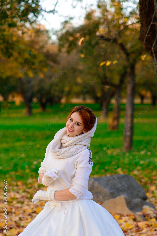 Cute girl in long white wedding dress posing in rural path among autumnal trees in forest in golden hour atmosphere. Cute girl in long white wedding dress posing in rural path among autumnal trees in forest in golden hour atmosphere.