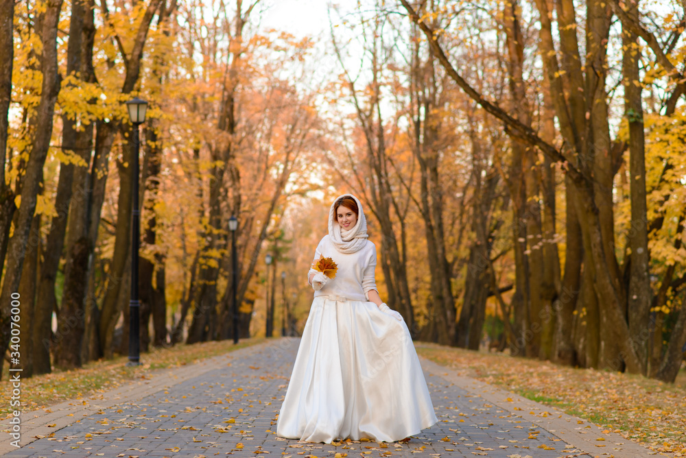 Cute girl in long white wedding dress posing in rural path among autumnal trees in forest in golden hour atmosphere. Cute girl in long white wedding dress posing in rural path among autumnal trees in forest in golden hour atmosphere.