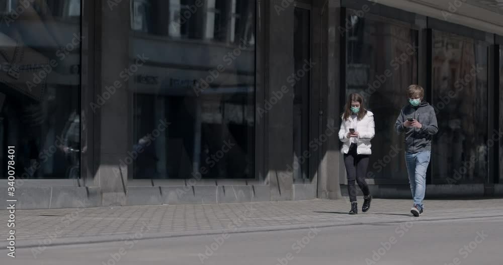 People spending more time online in time of coronavirus pandemic. Two people with medical masks walking side by side and being glued to their phones People spending more time online in time of coronavirus pandemic. Two people with medical masks walking side by side and being glued to their phones