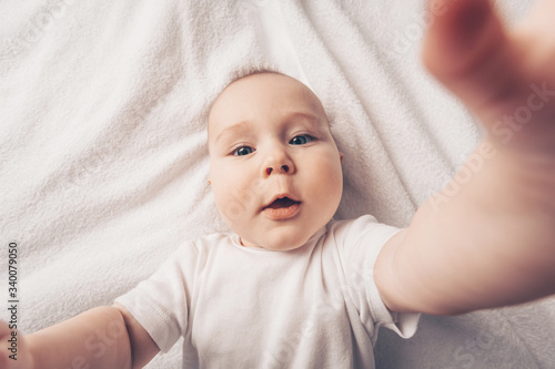 A little beautA little beautiful baby boy takes a selfie lying on a bed. Pulls his hands to the camera. photo