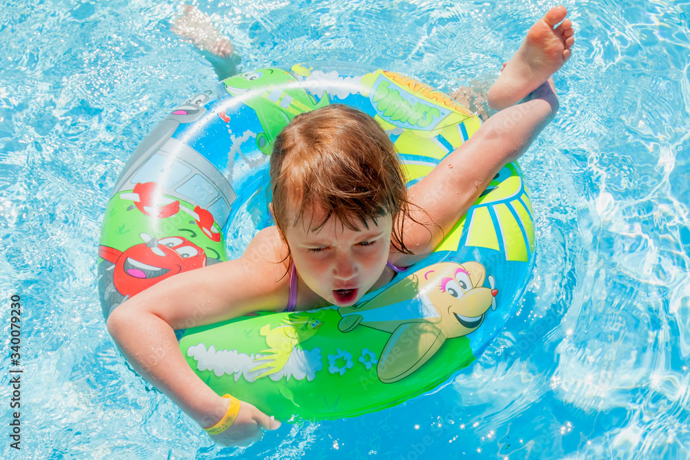 Young beautiful child girl splashing in swimming pool and having fun leisure activity