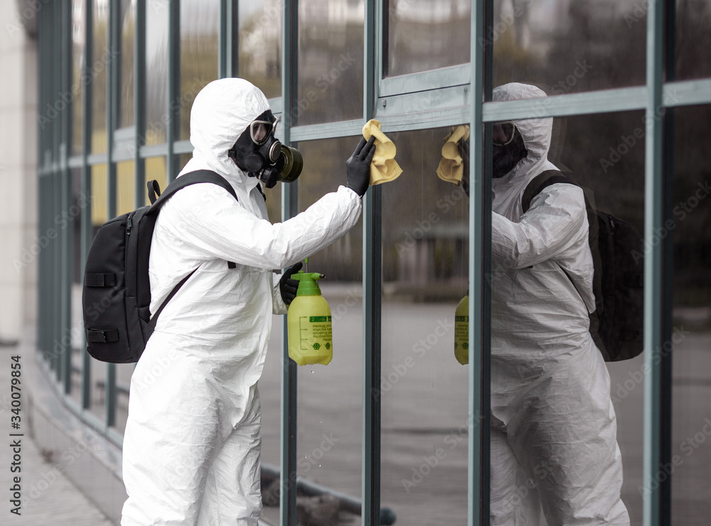 Fototapeta premium Quarantine, coronavirus infection. A man in protective equipment disinfects with a sprayer in the city. Cleaning and Disinfection at the street. Protective suit and mask. Epidemic.