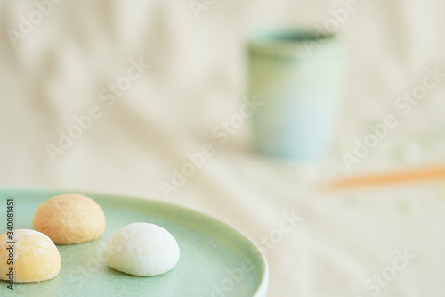 Three bright colorful mochis on a green plate and a coffee cup on a beige fabric.