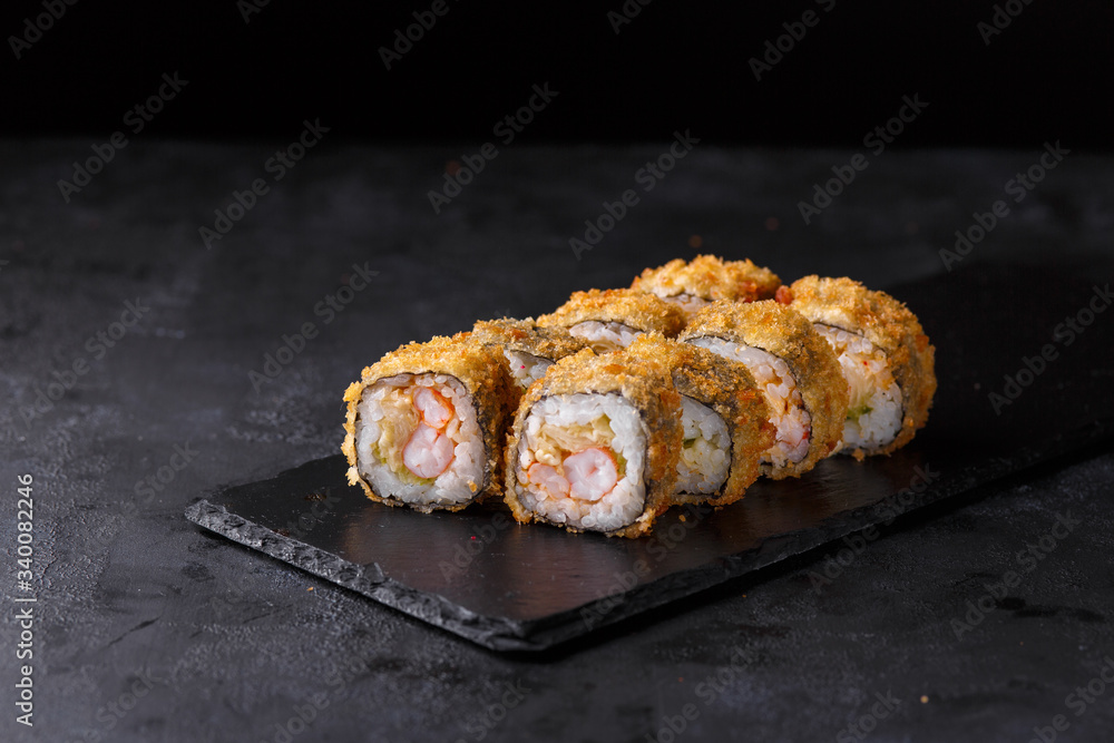 Sushi rolls with rice, nori, spicy sauce, cucumber, shrimp, masago on a black slate. Sushi rolls with rice, nori, spicy sauce, cucumber, shrimp, masago on a black slate.