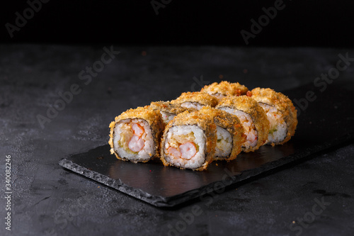 Sushi rolls with rice, nori, spicy sauce, cucumber, shrimp, masago on a black slate.