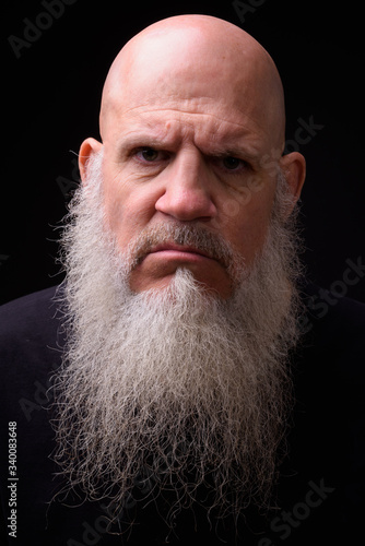 Mature bald bearded man against black background