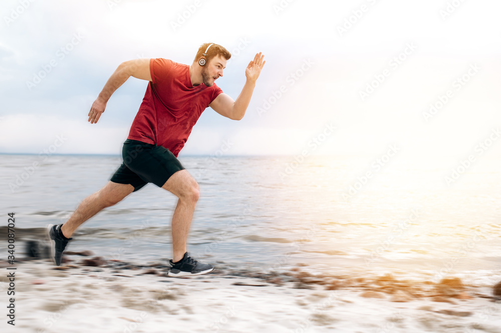 Runner in motion. Athletic guy in sportswear runs on the beach at sunset listening to his favorite music on headphones