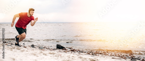 Sport lifestyle. Runner in motion. Athletic guy in sportswear runs very fast on the beach at sunset listening to his favorite music on headphones photo