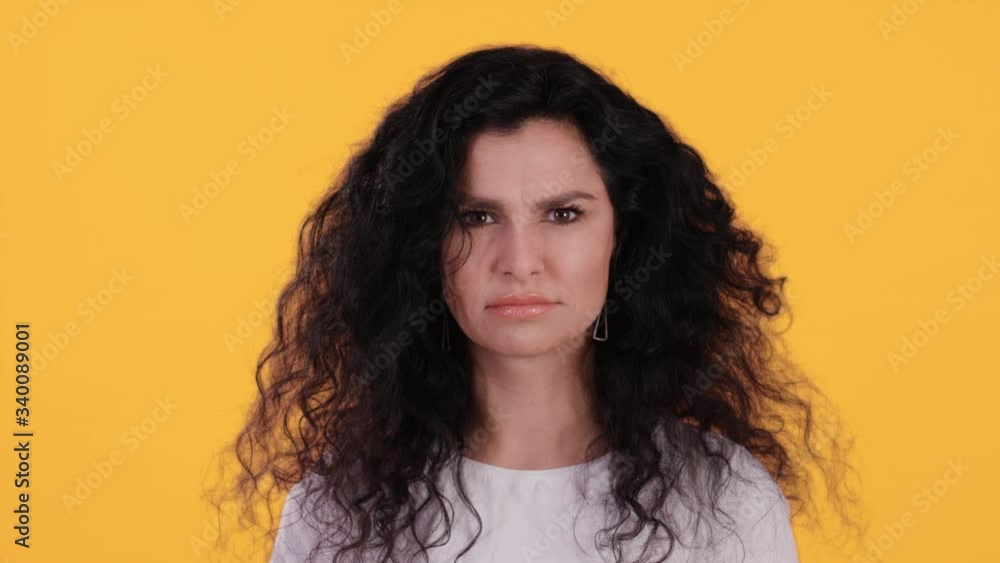 Portrait of beautiful young woman with black curly hair looking angry towards the camera and starting to smile and laugh isolated on yellow background shot in 4k Portrait of beautiful young woman with black curly hair looking angry towards the camera and starting to smile and laugh isolated on yellow background shot in 4k