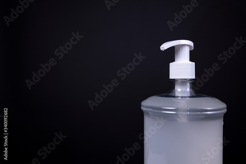 Bottle of plastic unmarked disinfecting sanitising hand gel consisting of a thick hazy non-transparent substance with white push faucet evenly lit in studio against a dark grey background photo