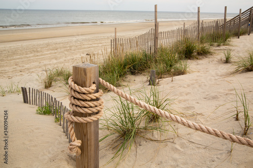 A Rope Barrier Wrapped Around a Post with Barrier Fences and Wild Grass on a Beach with Breaking Waves