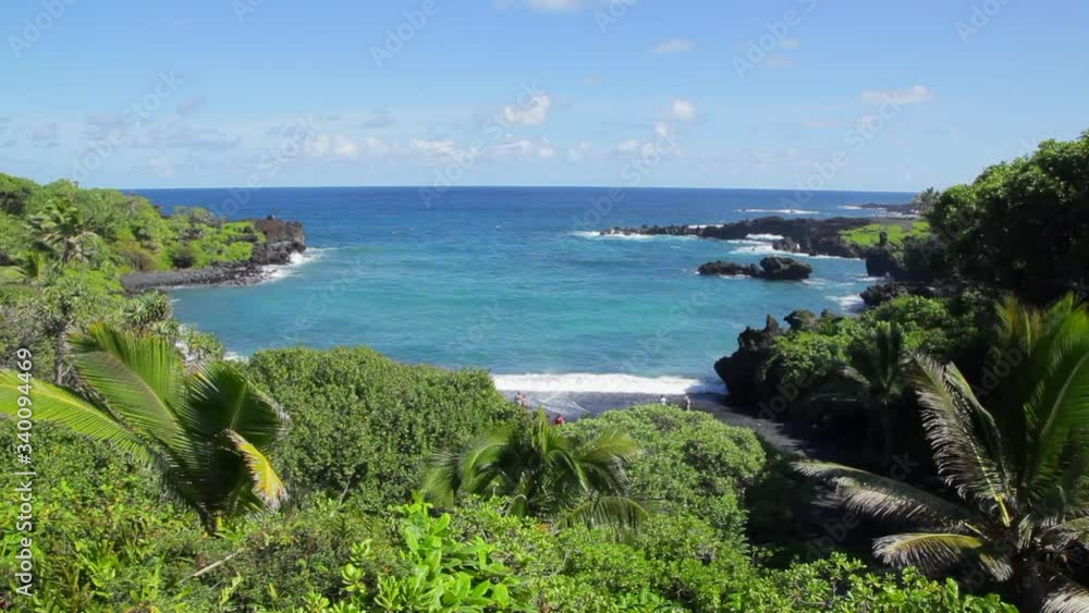 View of Pailoa Bay at Waianapanapa State Park on the drive to Hana on Maui with aqua ocean surrounded by jagged lava rock with black sand beach below on sunny blue-sky Hawaii day. View of Pailoa Bay at Waianapanapa State Park on the drive to Hana on Maui with aqua ocean surrounded by jagged lava rock with black sand beach below on sunny blue-sky Hawaii day.