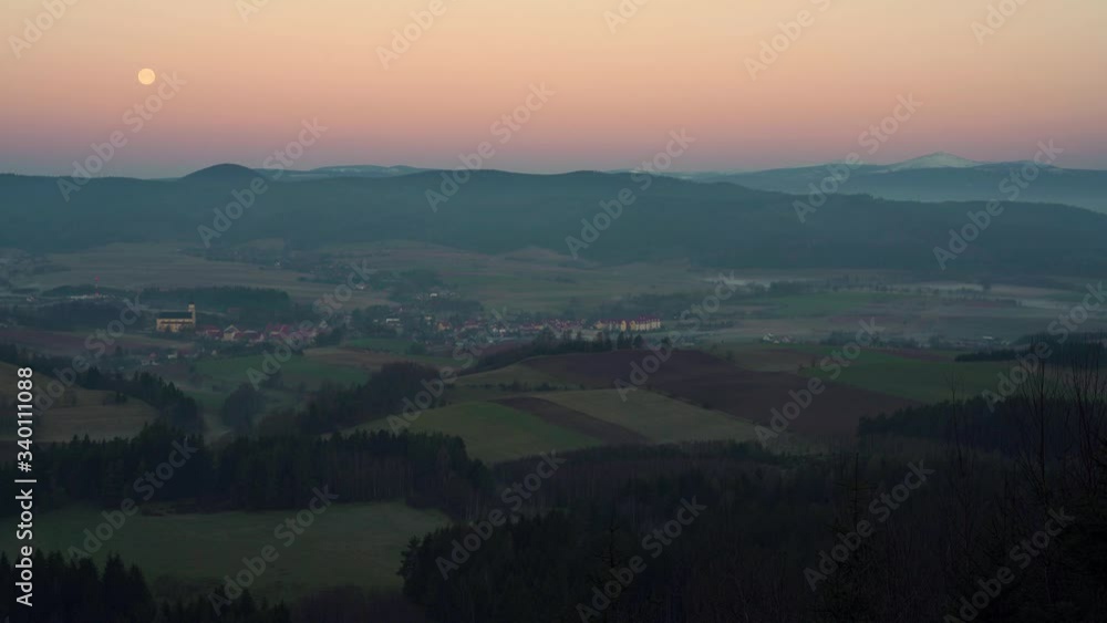 Sunrise in Chelmsko Slaskie. Full moon is visible on the horizon. Lower Silesia, Karkonosze Mountains. In the distance Śnieżka mountain visible. 4K footage. Sunrise in Chelmsko Slaskie. Full moon is visible on the horizon. Lower Silesia, Karkonosze Mountains. In the distance Śnieżka mountain visible. 4K footage.