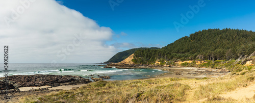 Panoramic view of a beach and green hills along the coast in Oregon with a fog bank offshore