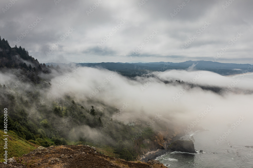 View of fog coming ashore over tree laden hills along the Oregon coast