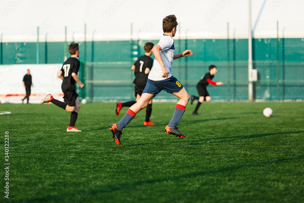 Boys in  white black sportswear running on soccer field. Young footballers dribble and kick football ball in game. Training, active lifestyle, sport, children activity concept
