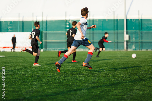 Boys in  white black sportswear running on soccer field. Young footballers dribble and kick football ball in game. Training, active lifestyle, sport, children activity concept © Natali