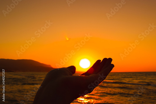 A hand holding a sun over a beautiful yellow sunset. The concept of the relationship/harmony between nature and humanity.
