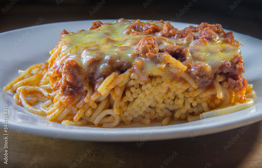 spaghetti bolognese with melted cheese on top, in a white plate and a black background spaghetti bolognese with melted cheese on top, in a white plate and a black background
