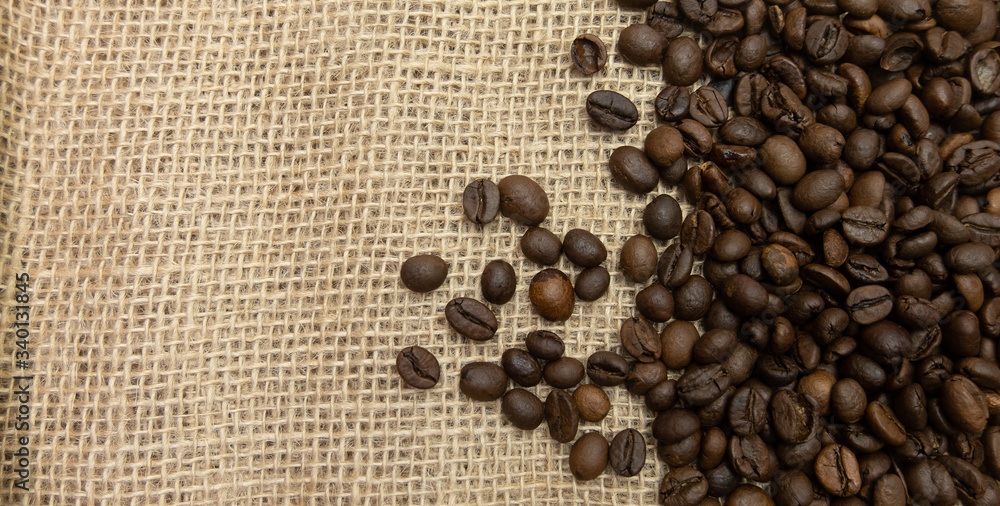Coffee beans spilled out onto burlap sack cloth with copy space on left Coffee beans spilled out onto burlap sack cloth with copy space on left