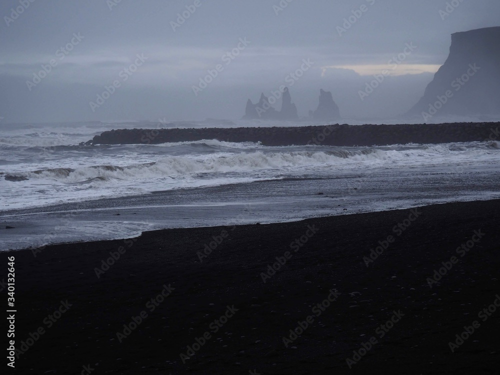A scenery of a South Iceland beach (Reynisfjara), black sand beach, foamy sea water, Rushing waves, Iceland South coast, basalt, rough sea, pale milky dim natural light, winter beach, monotone A scenery of a South Iceland beach (Reynisfjara), black sand beach, foamy sea water, Rushing waves, Iceland South coast, basalt, rough sea, pale milky dim natural light, winter beach, monotone