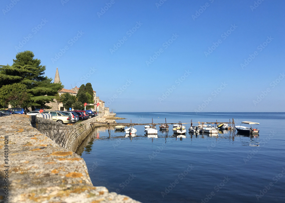 Boats docked along sit the old town or Stari Grad of Poreč Croatia along the Adriatic Sea against a clear blue sky.
