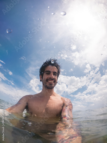 Selfie of  young man with tattooed arms swimming at the green and calypso ocean with cloudy blue sky, Riviera Maya coast, Mexico © Samuel Ponce
