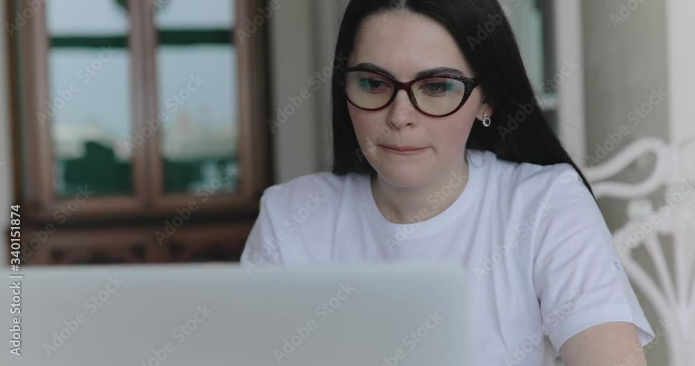 Thoughtful girl in glasses working with laptop at table in room Thoughtful girl in glasses working with laptop at table in room