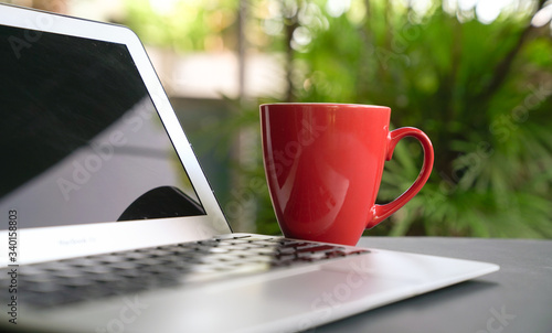 Computer laptop with offee in red cup with green nature background. Work remotely or from home. photo