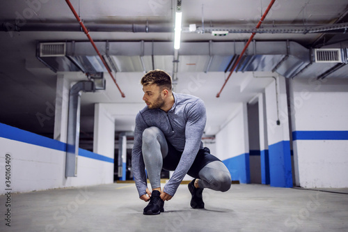 Young man crouching and tying shoelace in underground garage.