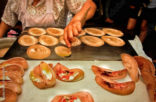 Street food vendor cooking and selling traditional thai crepes called khanom bueang showing the authentic streetfood and candid local experience in Thailand photo