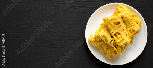 Homemade Net Crepe Roti Jala on a white plate on a black background, top view. Flat lay, overhead, from above. Space for text.