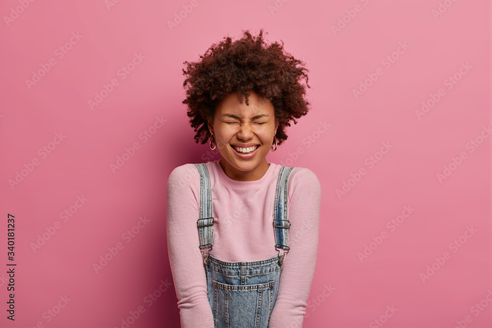 Beautiful carefree woman with toothy smile, laughs at something positive, expresses happiness, giggles over funny joke, wears turtleneck and overalls, makes happy reaction on something really good Beautiful carefree woman with toothy smile, laughs at something positive, expresses happiness, giggles over funny joke, wears turtleneck and overalls, makes happy reaction on something really good